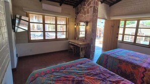 A room with two beds, a desk, and a stone wall.