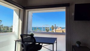 A balcony with a table and chair, a TV on the wall, and a view of the sea and buildings. - Suite Buenavista 301 y 302 (La Paz)
