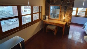 Une pièce avec un mur en pierre, un bureau en bois, une chaise, une fenêtre et un appareil de climatisation.