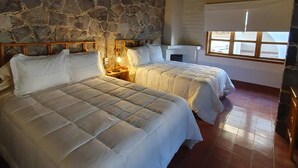 Ein Zimmer mit zwei Betten, Steinwänden, einer Holzbalkendecke und einem Fenster mit Jalousien.