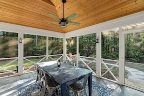 A covered patio with a table and chairs, large windows, and a ceiling fan. - Charming home near Clemson, SC! (Central)