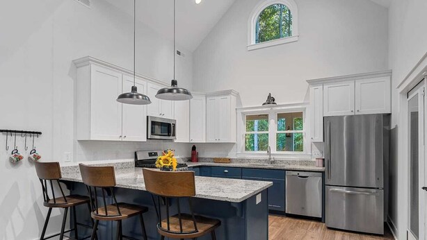 A modern kitchen with white cabinets, a stainless steel refrigerator, and a large island with bar stools. - Charming home near Clemson, SC! (Central)