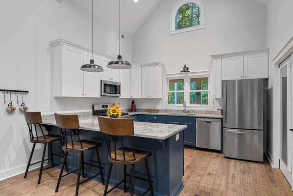 A modern kitchen with white cabinets, a stainless steel refrigerator, and a large island with bar stools. - Charming home near Clemson, SC! (Central)