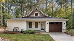 A single-story house with a gabled roof, a front garage, and a small porch with a wheelbarrow. - Charming home near Clemson, SC! (Central)