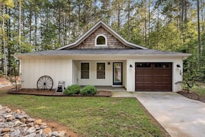 A single-story house with a gabled roof, a front garage, and a small porch with a wheelbarrow. - Charming home near Clemson, SC! (Central)