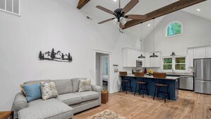 A spacious living area with a sofa, a coffee table, a ceiling fan, and a kitchen with a bar area. - Charming home near Clemson, SC! (Central)
