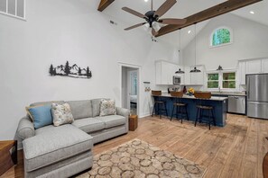 A spacious living area with a sofa, a coffee table, a ceiling fan, and a kitchen with a bar area. - Charming home near Clemson, SC! (Central)