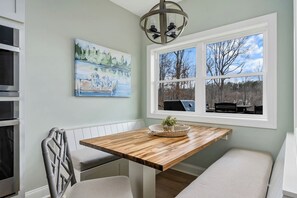 Ein Essbereich mit einem Holztisch, einer Bank, einem Bild an der Wand und Blick durch ein Fenster.