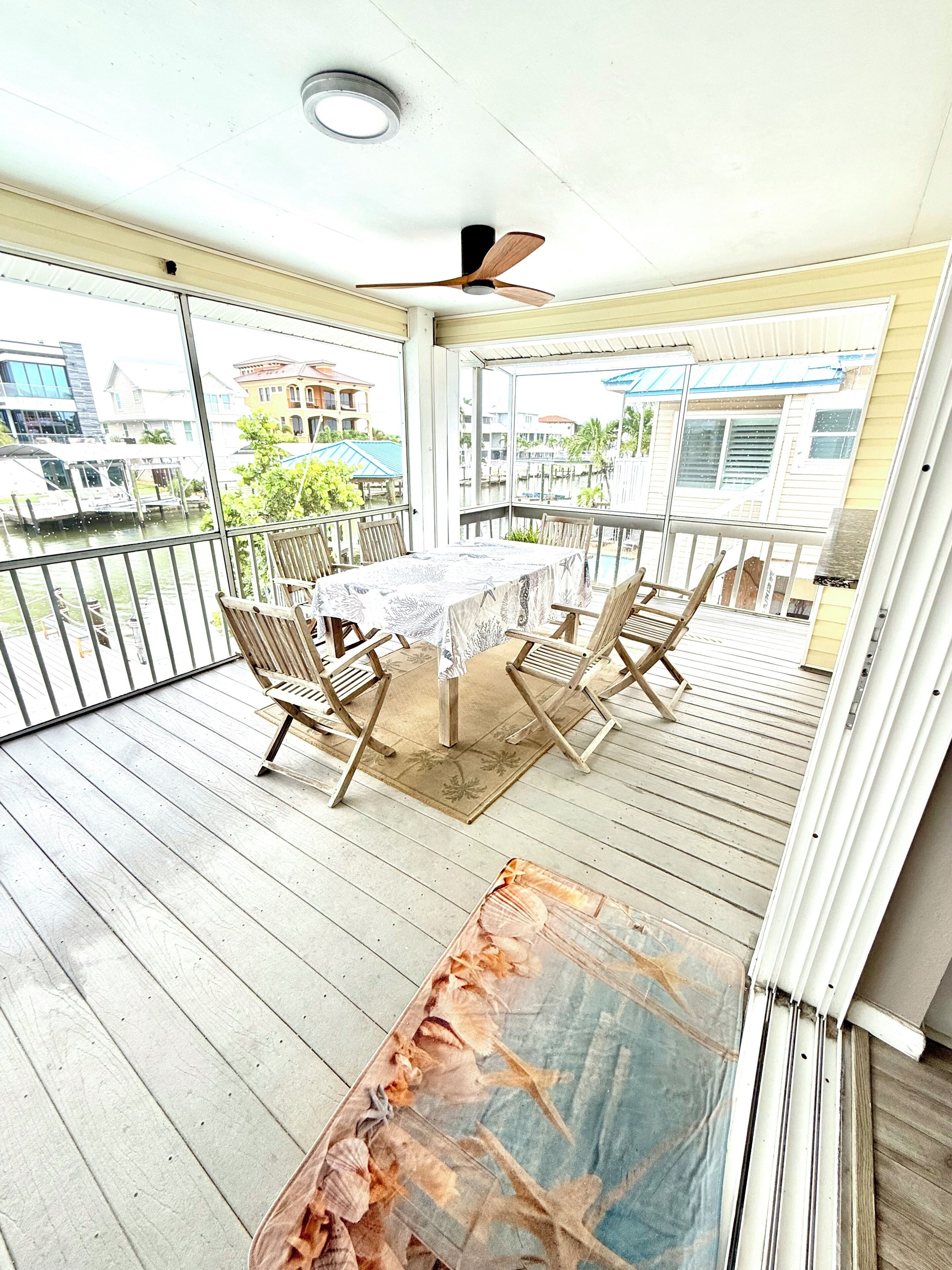 A covered outdoor area with a table and chairs, a ceiling fan, and a view of the surrounding area.