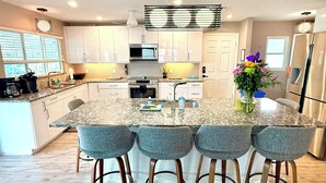 A modern kitchen with a central island, bar stools, stainless steel appliances, and a large window. - Private Canal Retreat - Heated Pool & Spa (Fort Myers Beach)