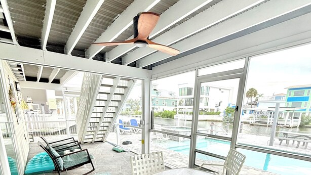 A covered outdoor area with a pool, white furniture, and a view of buildings and water. - Private Canal Retreat - Heated Pool & Spa (Fort Myers Beach)
