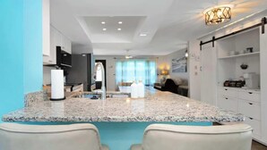 A modern kitchen with granite countertops, white cabinetry, and a central island with seating. - Luxurious New Heated Pool & Spa! 4 mins to beach! (Seminole)