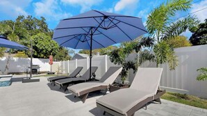A patio with lounge chairs and a large umbrella. - Luxurious New Heated Pool & Spa! 4 mins to beach! (Seminole)