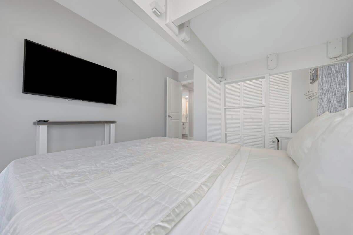 Une chambre à coucher avec un lit, un téléviseur fixé au mur et une porte donnant sur une autre pièce.