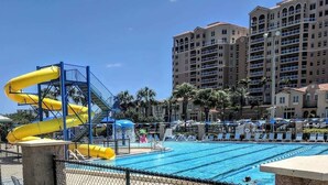Ein Schwimmbecken mit Wasserrutsche, Liegestühlen und einem hohen Hotel im Hintergrund.