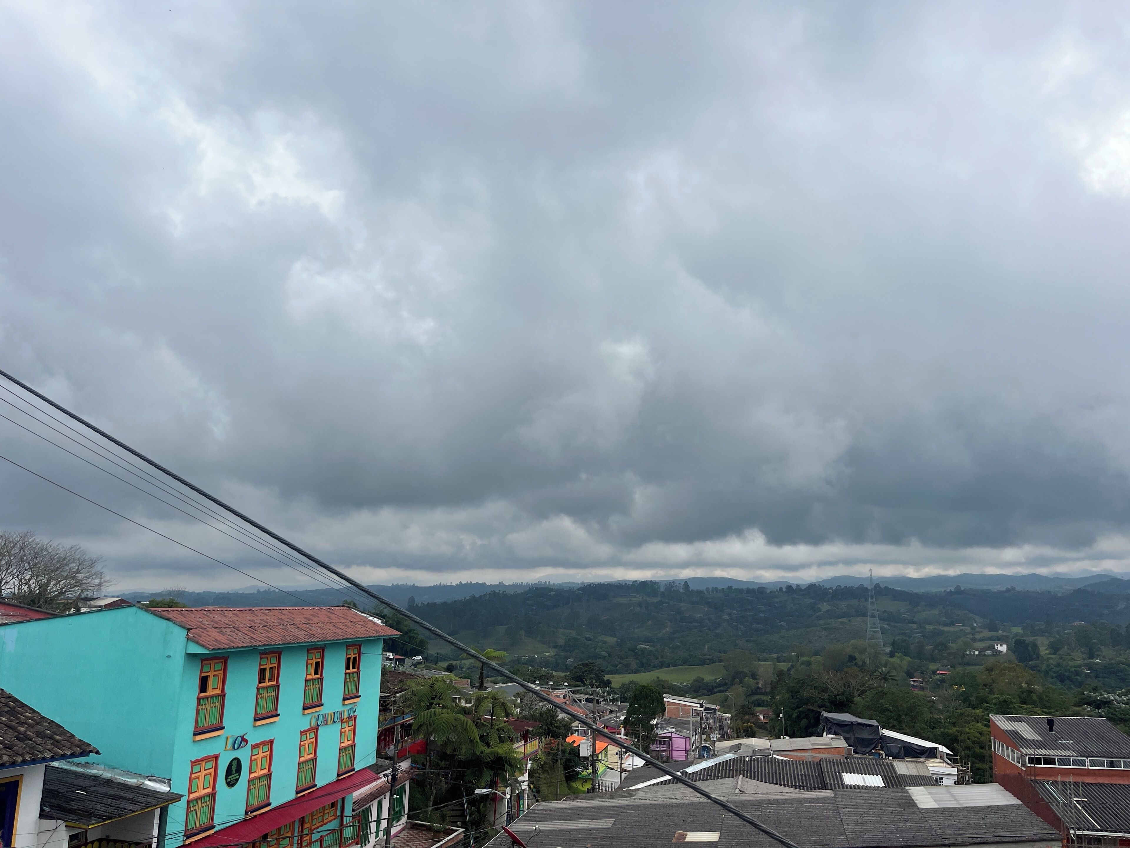 A residential area with colorful buildings, a hilly landscape, and a cloudy sky.