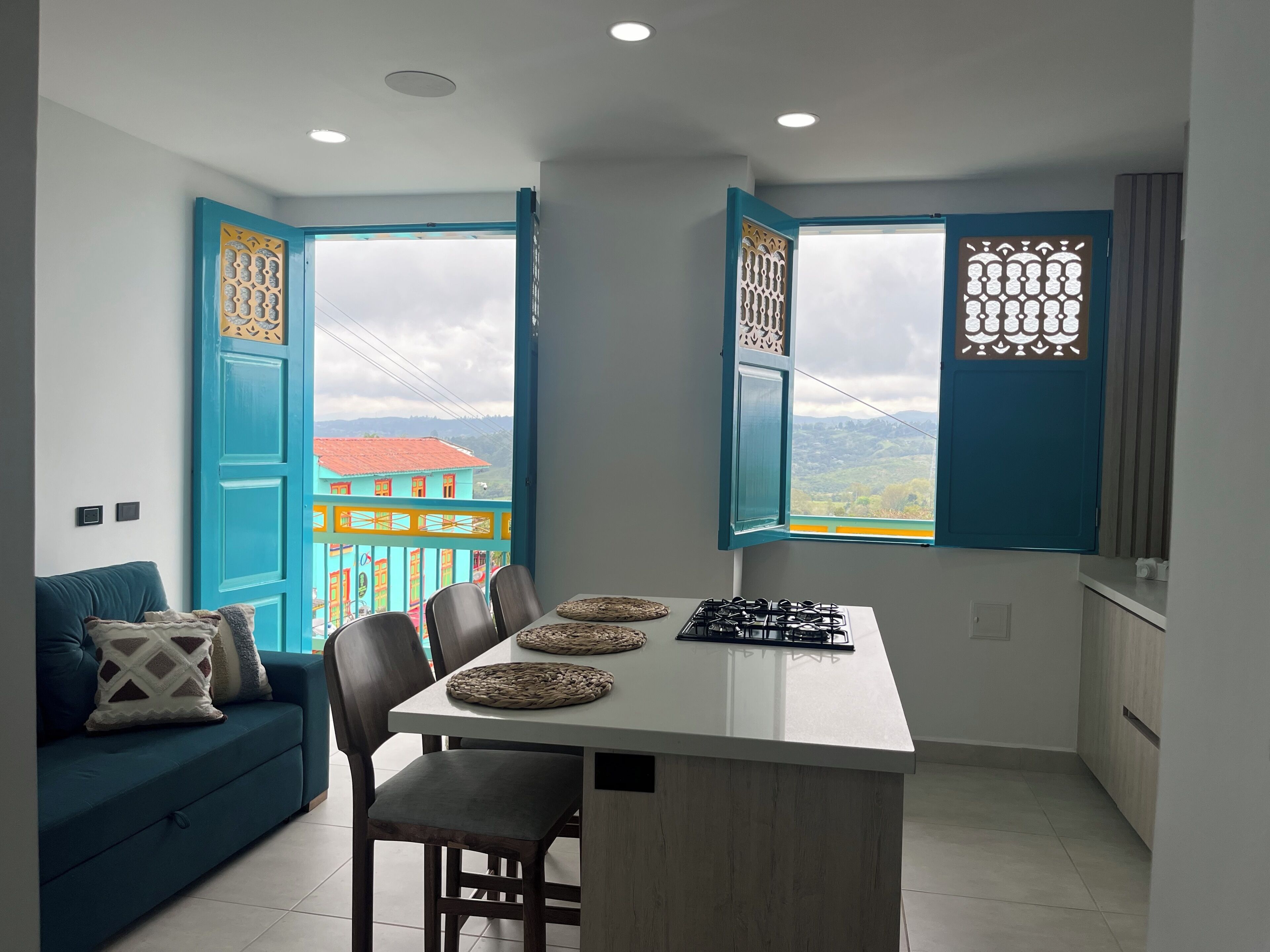 Cozinha compacta com área de refeições, um sofá e vista para um edifício com telhado vermelho.