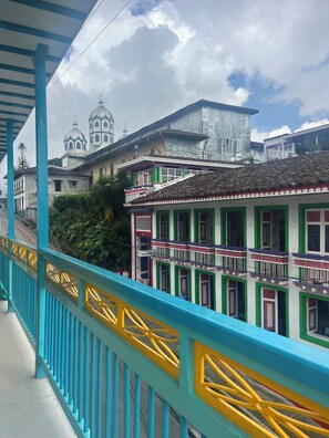 Un edificio colorido con balcones, una barandilla azul y amarilla, y una iglesia con cúpulas al fondo.
