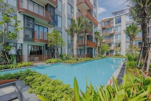 A modern hotel with a central swimming pool surrounded by lush greenery and multiple balconies. - Cozy 2br Apartment Pool View- canvas- bangtao area (Choeng Thale)