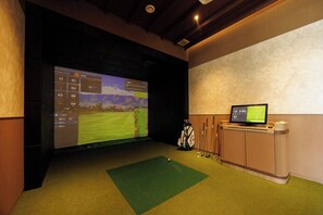 A room with a large screen displaying a golf course, a golf bag, and several golf clubs. - Cozy 2br Apartment Pool View- canvas- bangtao area (Choeng Thale)