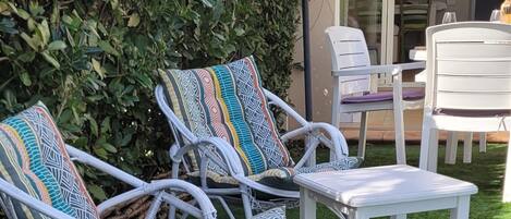 Outdoor wicker furniture with patterned cushions, a white table, and a blue umbrella on a well-maintained lawn.
