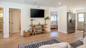 Un soggiorno moderno con televisore piatto, mobile TV in legno e un grande frigorifero.