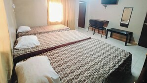 Ein Hotelzimmer mit zwei Betten, einem Schreibtisch, einem Sessel, einem Fernseher und einem Spiegel.