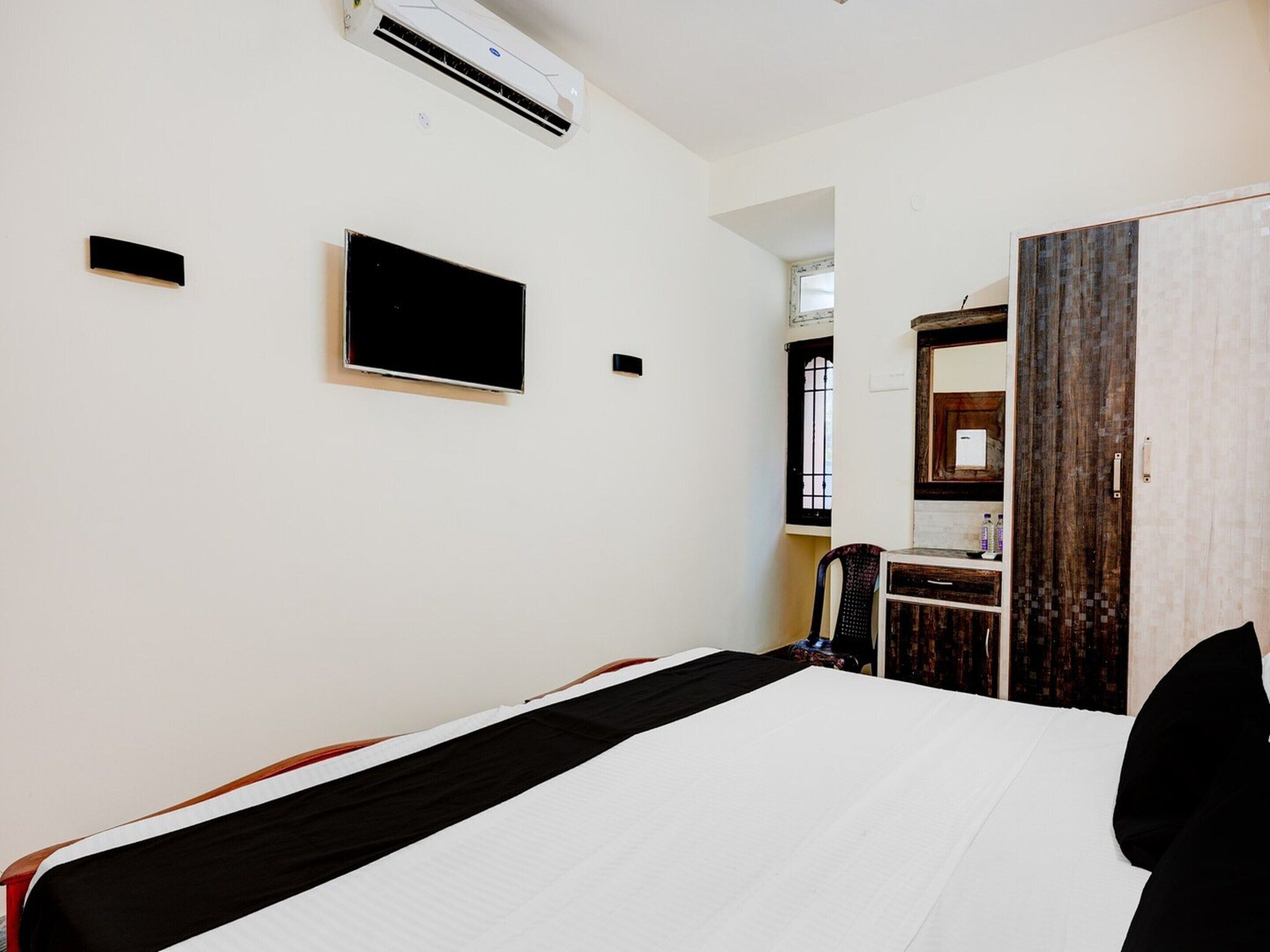 A hotel room with a bed, a flat-screen TV, an air conditioning unit, a desk with a chair, and a wardrobe.