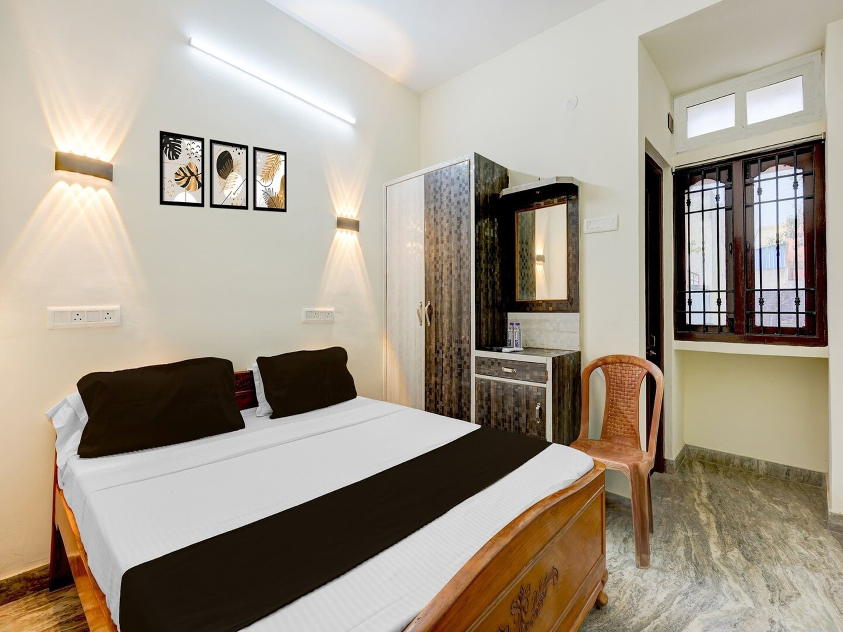 A bedroom with a bed, bedside lamps, a wardrobe, a mirror, and a window with bars.