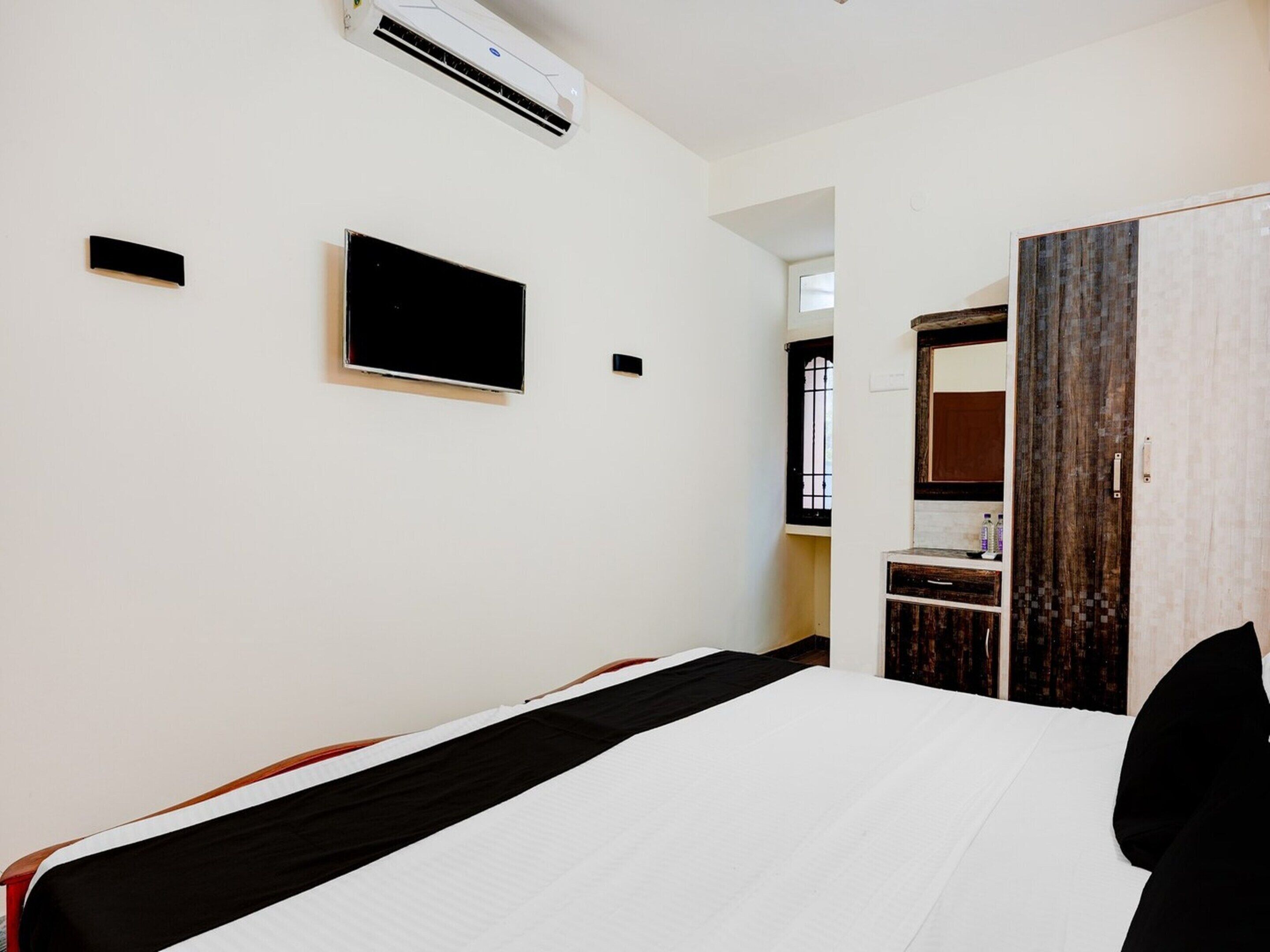 Habitación de hotel con cama, televisor de pantalla plana, aire acondicionado, armario y baño con espejo y lavabo.