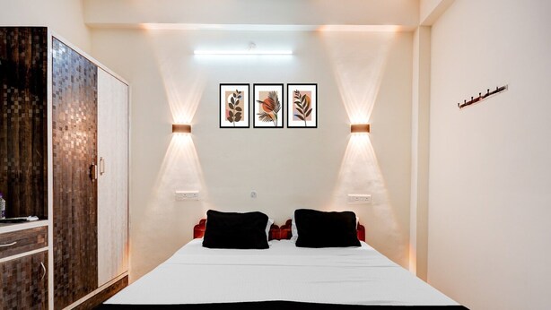 A hotel room with a bed, two bedside tables, a wardrobe, and wall-mounted artwork. - Deluxeannakilly Tower Guest House (Chennai)