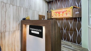 Ein Empfangsschalter mit der Aufschrift 'Townhouse' und einem Schild 'Dienstanweisungen', ein dekorativer Gegenstand darauf sowie eine Wand mit Muster im Hintergrund.