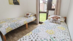 A bedroom with two single beds, a wooden floor, a door to a garden, and a painting on the wall. - Tolroy Manor Holiday Park (Hayle)