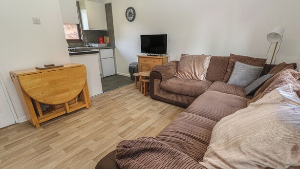 A living room with a sofa, a wooden table, a television, and a kitchen area in the background. - Tolroy Manor Holiday Park (Hayle)
