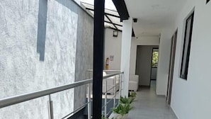 Un pasillo con barandilla de metal, plantas en macetas y pared blanca.