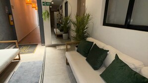 Un interior moderno con un sofá blanco, cojines verdes, una planta en maceta y un ventanal grande.