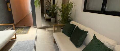 Un interior moderno con un sofá blanco, cojines verdes, una planta en maceta y un ventanal grande.