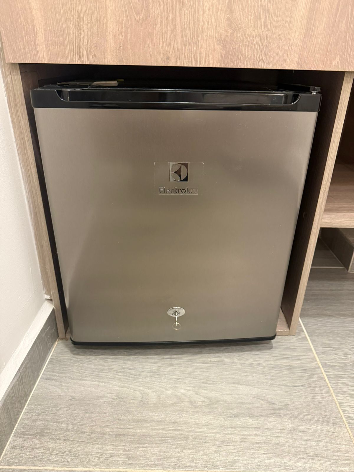 Ein kompakter, dunkel gefärbter Kühlschrank mit sichtbarem Markenlogo, unter einem Holzkasten in einer Küche platziert.