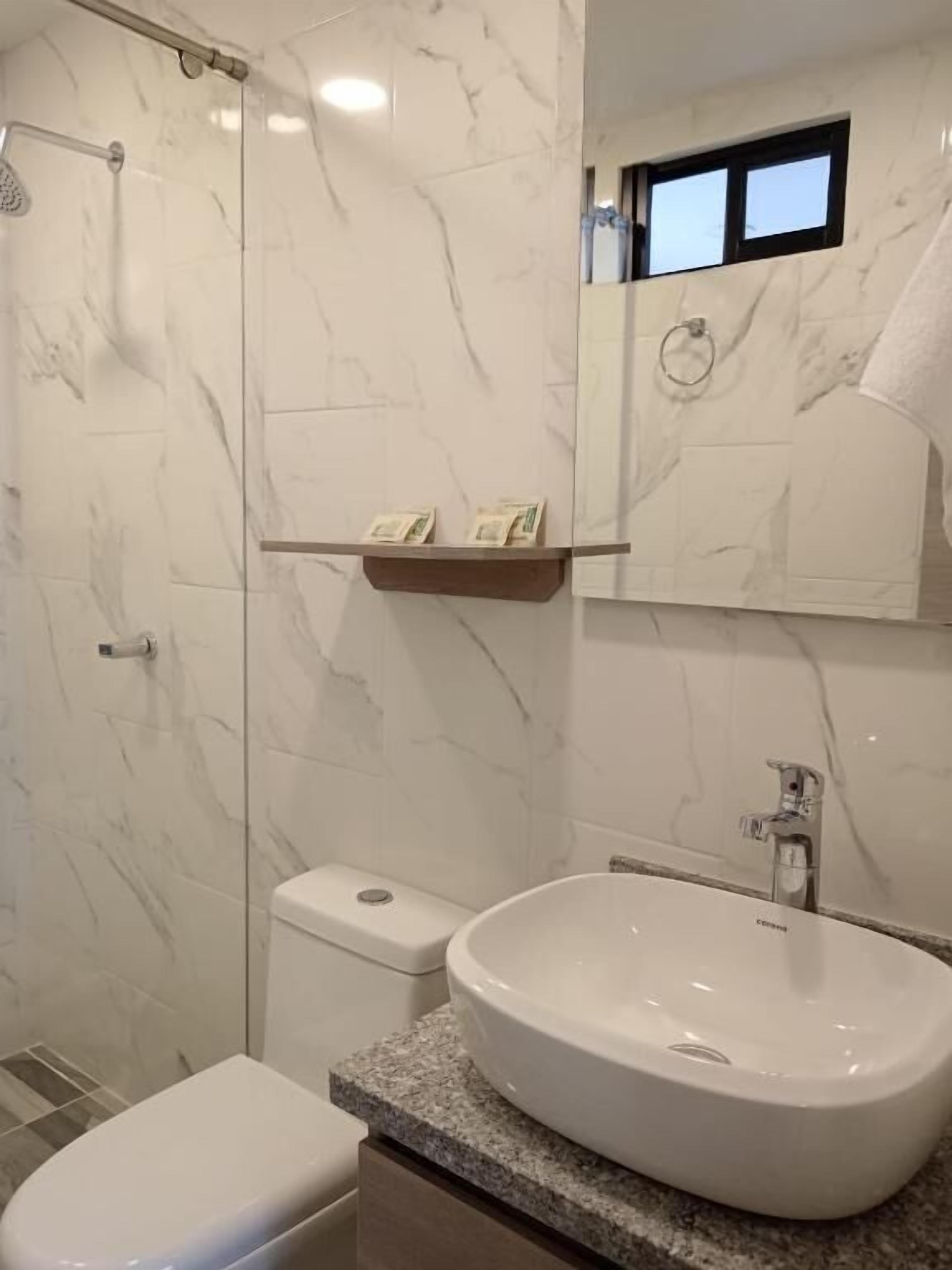 A bathroom with a marble wall, a toilet, a sink, and a shower.