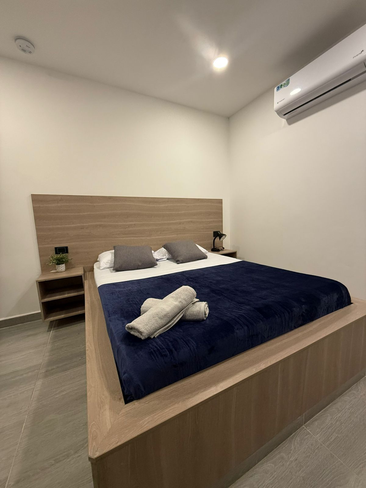 A modern bedroom with a large bed, a bedside table, a nightstand, and an air conditioning unit.
