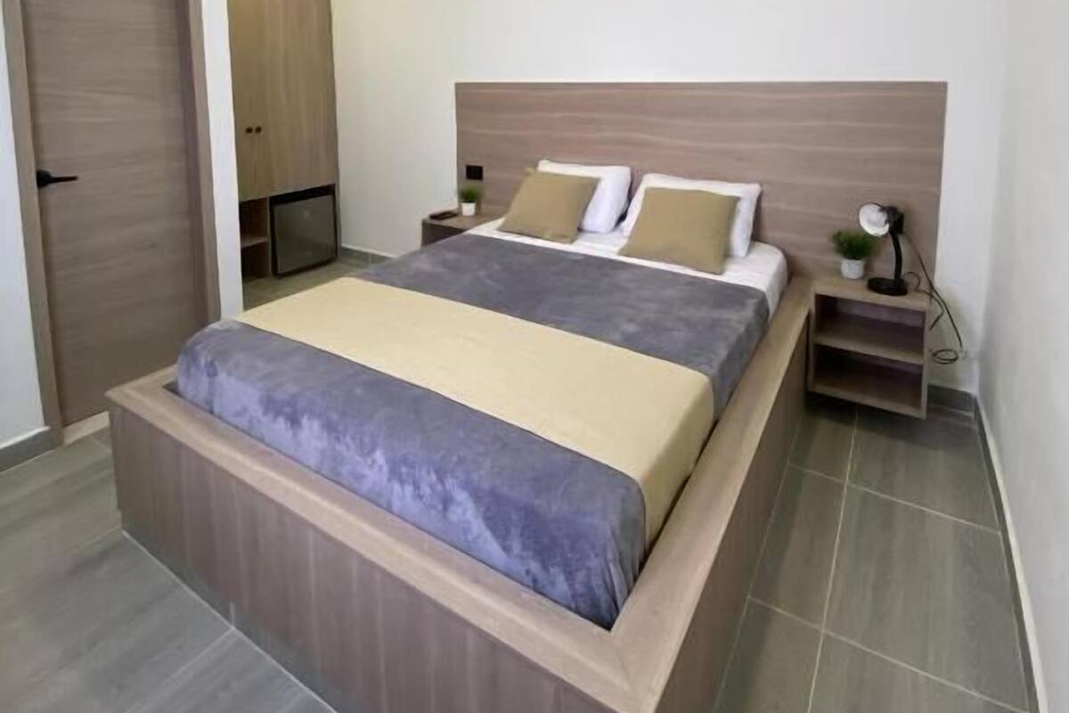 A modern bedroom with a large bed, a wooden wardrobe, and a nightstand with a lamp.