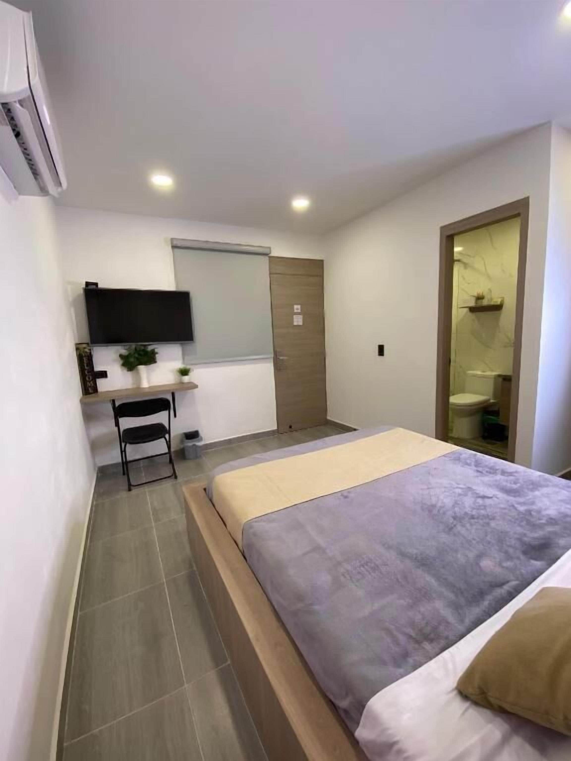 Un dormitorio con una cama, un escritorio, una silla, un televisor y una puerta.