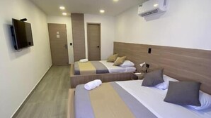 Habitación de hotel con dos camas, televisión, aire acondicionado y una puerta.