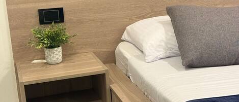 A bed with a headboard, a bedside table with a plant, and a power outlet.