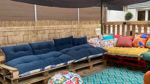 A wooden deck with a sofa and ottomans, a patterned rug, and a bamboo fence.