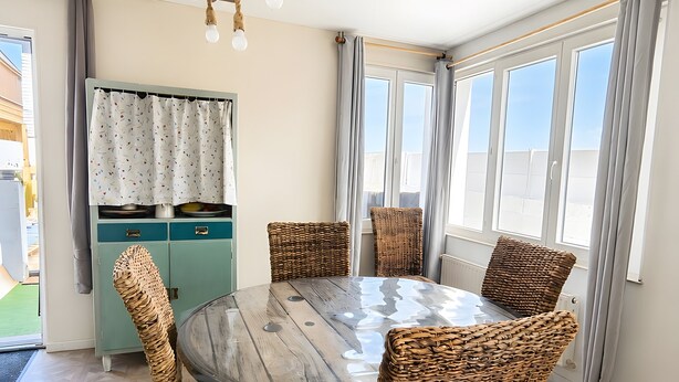 A dining area with a round table, wicker chairs, a light blue cabinet, and a hanging light fixture.