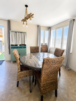 Un coin repas avec une table ronde, des chaises en osier, un buffet bleu clair et un luminaire suspendu.