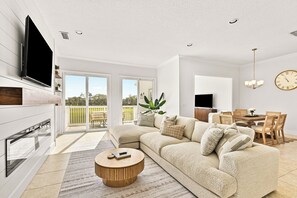 Een moderne woonkamer met een hoekbank, een flatscreen televisie, een eethoek en een grote schuifpui naar buiten.
