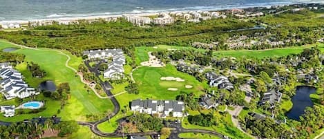 Vista aérea de un campo de golf con edificios residenciales, una piscina y vistas al océano.