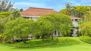 A two-story building with a red-tiled roof, surrounded by lush greenery and a well-maintained lawn. - Kiahuna #44 • A/C • REMODELED & UPDATED Ground-Floor End Unit • 2 Min to Beach (Koloa)